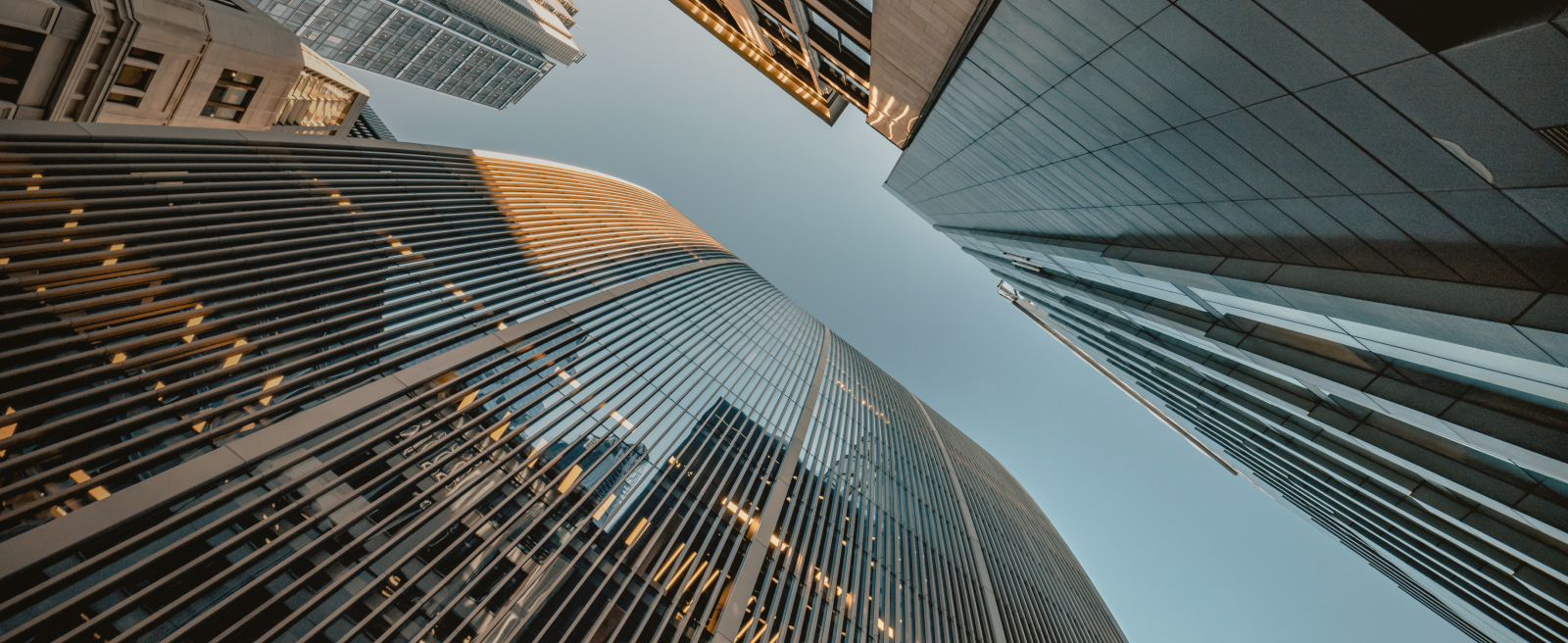 Upward view of several modern skyscrapers with clear blue sky in between.
