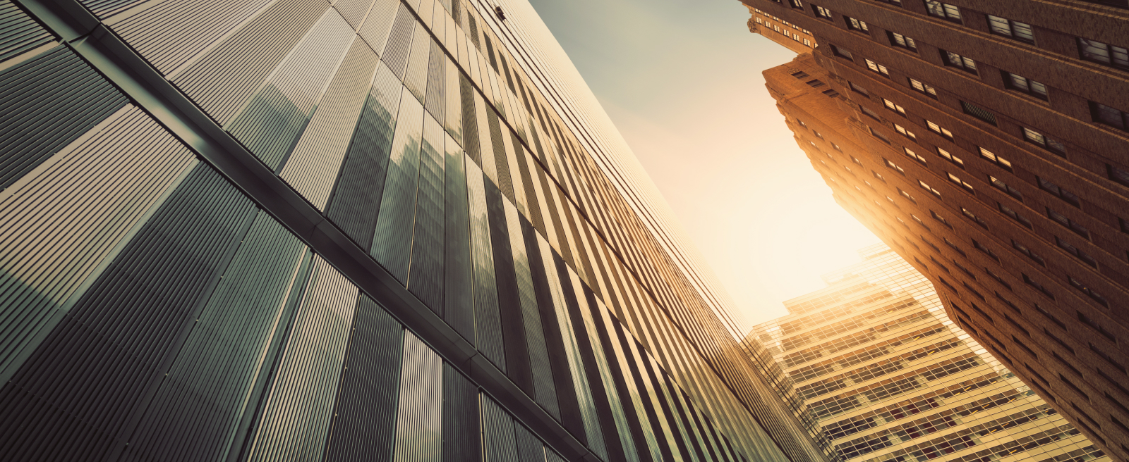 View from below of three tall buildings in North America with sun shining between them.