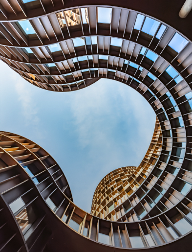 Upward view of a curvilinear modern building found in Denmark, revealing a partly cloudy sky.